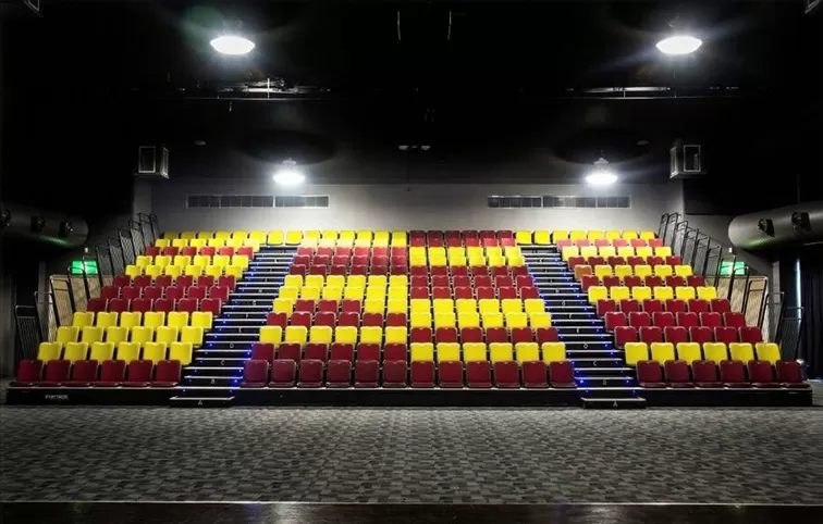 Empty auditorium with red and yellow retractable bleachers, modern event venue interior with flexible seating